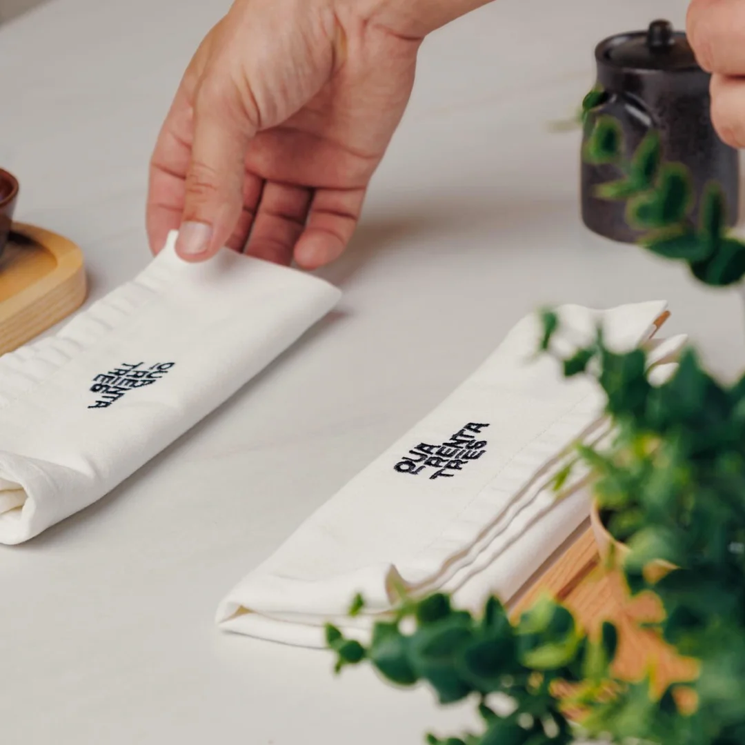 Projeto Quarenta e três da Nhdesign: Mão a colocar guardanapo com identidade visual Quarenta e Três sobre mesa de refeição