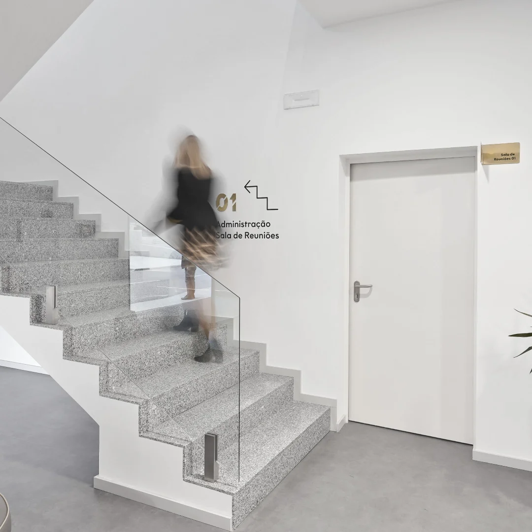 Projeto Inovocorte da Nhdesign: Mulher a subir escadas num edifício moderno de paredes brancas