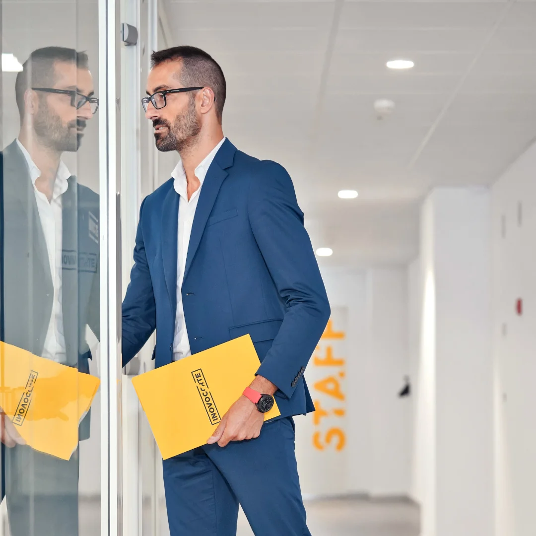 Projeto Inovocorte da Nhdesign: Colaborador da Inovocorte de fato azul a segurar pastas amarelas, refletido num vidro