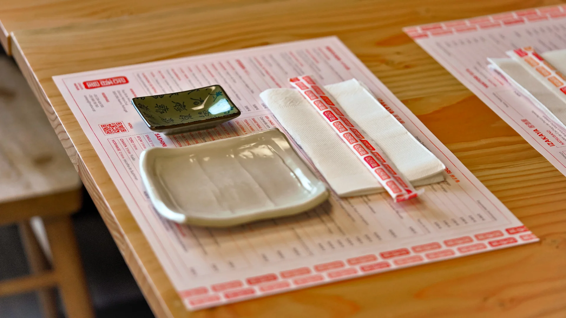 Projeto Izakaya Matsuri da Nhdesign: Prato, tigela e pauzinhos dispostos ordenadamente numa mesa com pauzinhos e individual de marca.