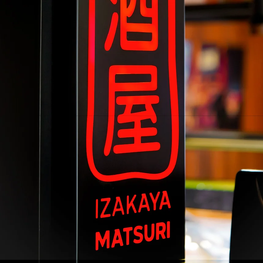 Projeto Izakaya Matsuri da Nhdesign: Fotografia em close-up de um letreiro luminoso com o logótipo no balcão de um bar.