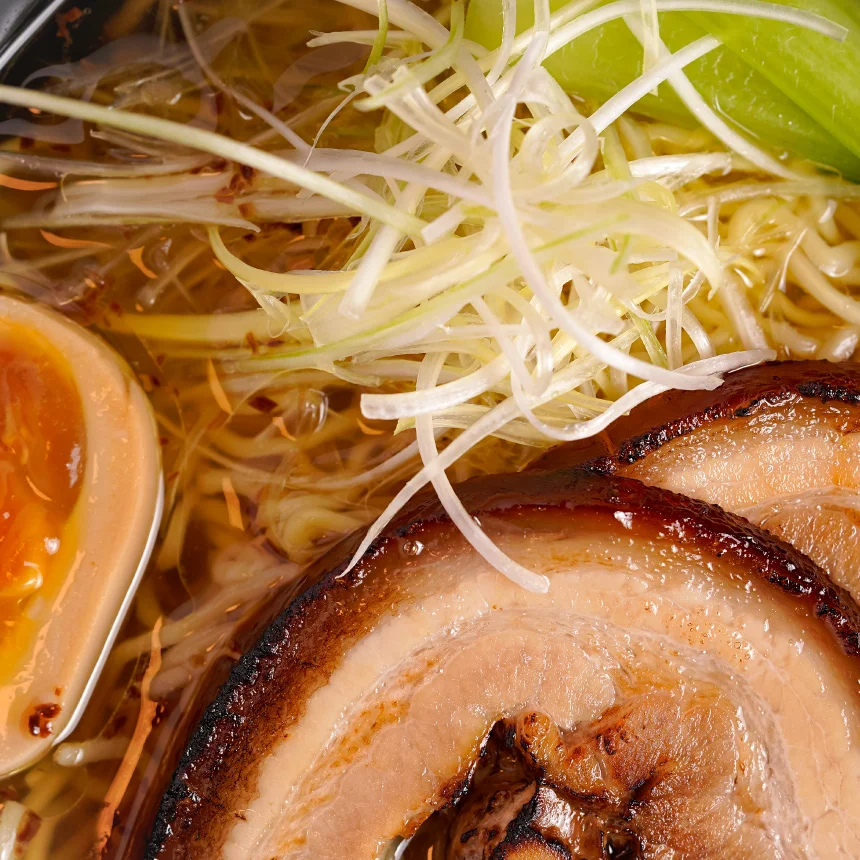 Projeto Izakaya Matsuri da Nhdesign: Fotografia em close-up de uma tigela de ramen com carne e vegetais misturados sobre uma mesa de madeira.